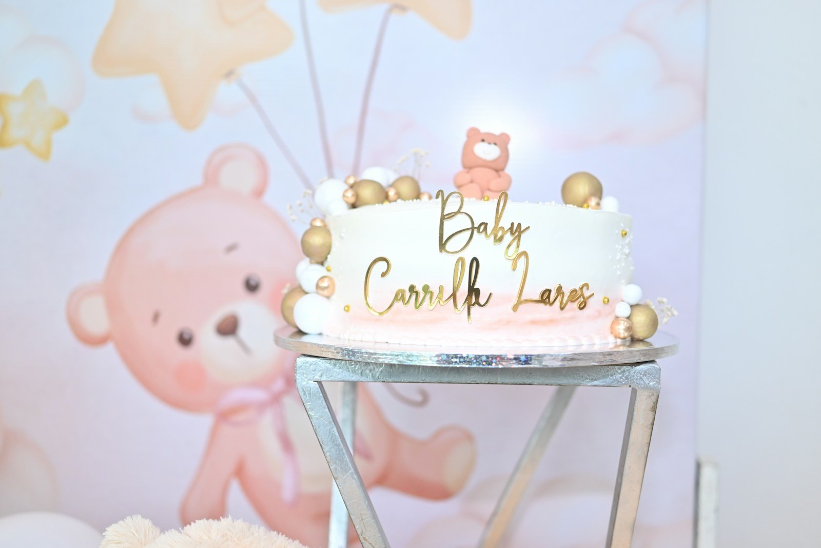 White cake with gold accents and teddy bear theme.